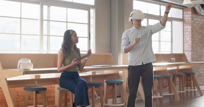 Diverse coworkers tapping tablet initiating coworker gesturing with VR headset testing at bar table