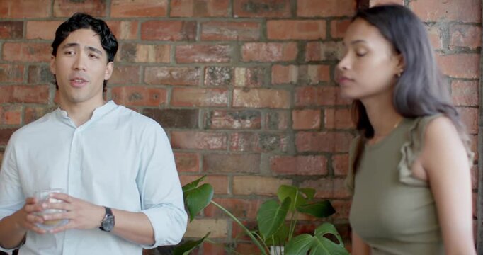 Diverse coworkers standing by brick wall, man holding glass speaking, leading woman reading phone