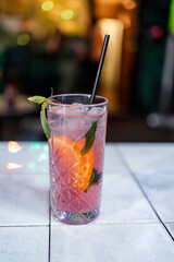 Refreshing drink with fruit in a clear glass on a table in a lively bar setting © Marko