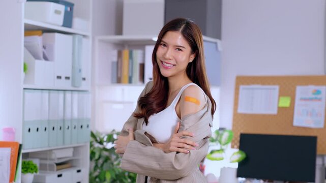 Asian young woman portrait with bandage on shoulder, smile in office workspace, cardigan style, self care health, hygiene, vaccine aftercare, cheerful employee near desk