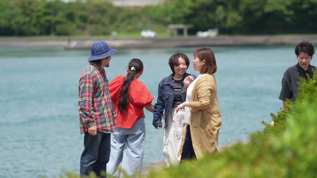 Five people stand by a calm blue lake. One woman points toward the water, smiling. Another laughs, arms outstretched joyfully. They appear relaxed and happy, enjoying the moment. Perfect for vacation