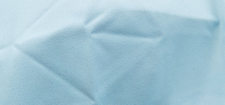 Surface texture of grayish-light blue synthetic leather or thick fabric material with sharp geometric folds