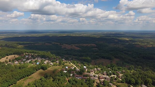 aerial countryside landscape with forests, fields, and small village under blue sky