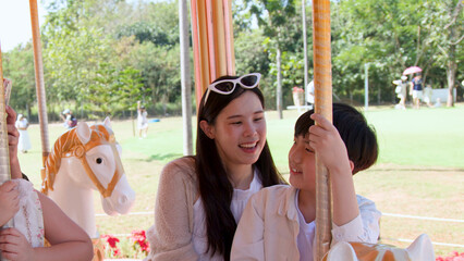 Happy Asian Mother and Son Riding a Carousel Outdoors © blueringmedia