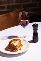 Naklejka premium Angled shot of beef lasagna slice with a glass of red wine and pepper mill, restaurant table setting