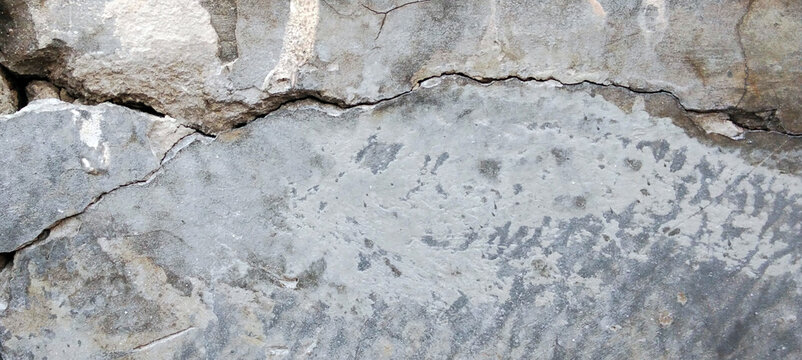 Texture of a gray concrete foundation that is severely cracked and broken.