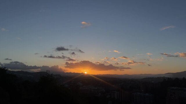 Golden sunset over city skyline with mountains and clouds