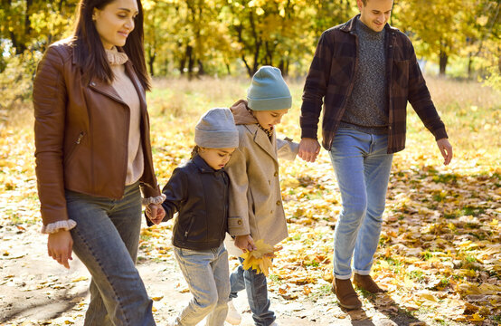Family with children walk together in autumn. Parents, mother and father, guide kids through a park with golden leaves, enjoying fresh air and weekend relaxation. Warm family joy and unity.