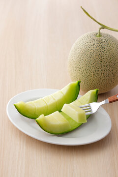 木目テーブルに置いた高品質な北海道産の青肉カットメロン　Slices of high-quality green flesh Japanese melon on a wooden table, premium Hokkaido muskmelon