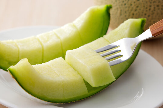 木目テーブルに置いた高品質な北海道産の青肉カットメロン　Slices of high-quality green flesh Japanese melon on a wooden table, premium Hokkaido muskmelon