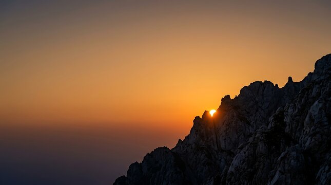 Golden sun rising behind a silhouetted rocky mountain ridge