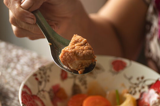 Metal spoon lifting a tender juicy chunk of cooked stewed pork or beef meat from a savory soup bowl close up
