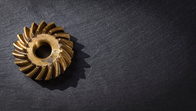 Bronze helical gear sitting on a dark textured slate surface