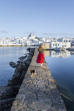 Cat and young woman with red dress on harbour wall, behind church of Naoussa, harbour town Naoussa, island Paros, Cyclades, Greece