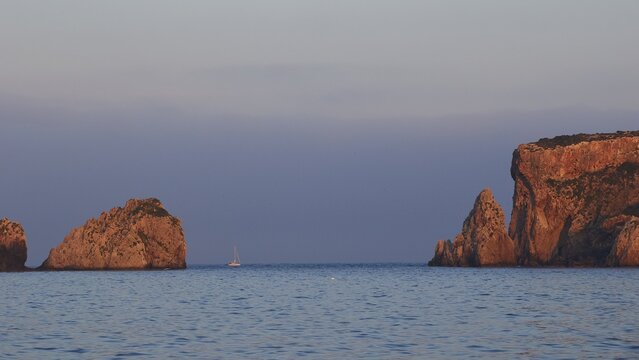 Sunrise over the sea with sailboat and rock formations, morning light, Tsichli Babas islet, Sfaktiria island, Navarino Bay, Pylos, Peloponnese, Greece