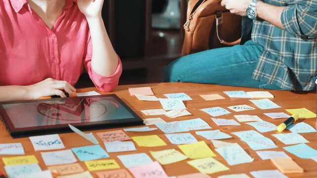 Close up of project manager hands shaking hand with businessman at meeting table with sticky notes and tablet displayed logo design. Business team working together and talking about idea. Symposium.