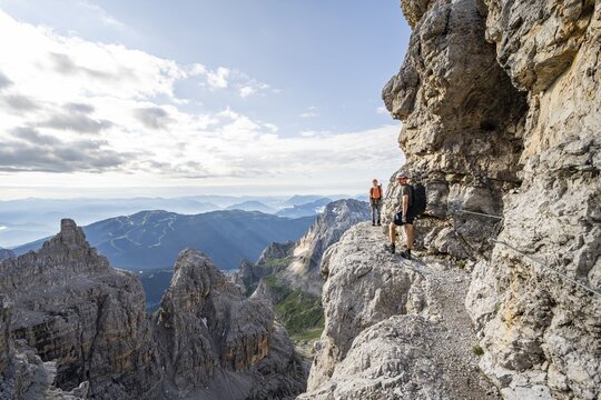 Two mountaineers climb an exposed rock band in the secured Via Ferrata Bocciere Centrale via ferrata, Brenta Mountains, Parco Naturale Brenta-Adamello, Trentino, Italy