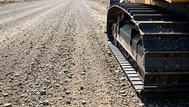 Heavy duty machinery metal tracks driving on rural gravel road surface at industrial construction zone site outdoors