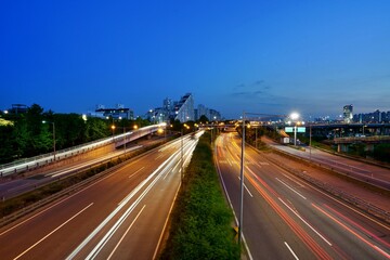 Fototapeta premium A symmetric high-angle twilight view of a multi-lane highway system with white and red traffic light trails branching through urban infrastructure.