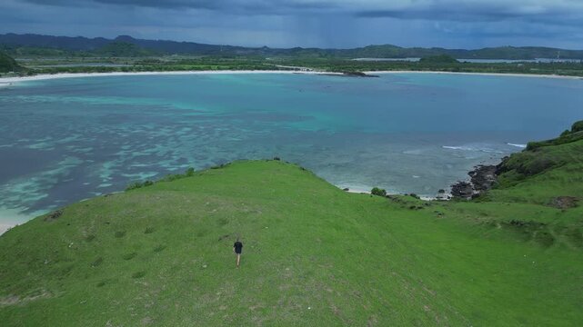 Woman Resting On Hilltop Overlooking Turquoise Bay And Narrow Headland Seated Figure Gazes At Calm Water, Soft Light,Aerial Composition Evokes Peace And Contemplation, Bukit Merese,Lombok, Tanjung Ann