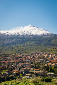Snow-capped Mount Etna with a summit steam plume rising above a Sicilian hill town in spring, Sicily, Italy