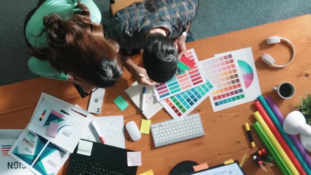 Top down view of smart designer helping manager choosing color from colored palettes. Aerial view of businessman working together and planning together while looking at logo from laptop. Symposium.