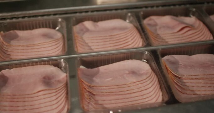 Stacked slices of ham lie in clear plastic trays on a production line in a meat packaging facility