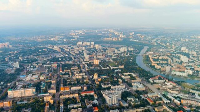Oryol, Russia. Sweeping aerial panorama over the historic city center, the winding Orlik River, and the broad tree-lined urban grid stretching toward a hazy summer horizon under soft cloudy skies. Dr