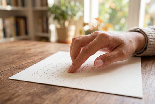 Hand reading a document written in braille on a wooden table