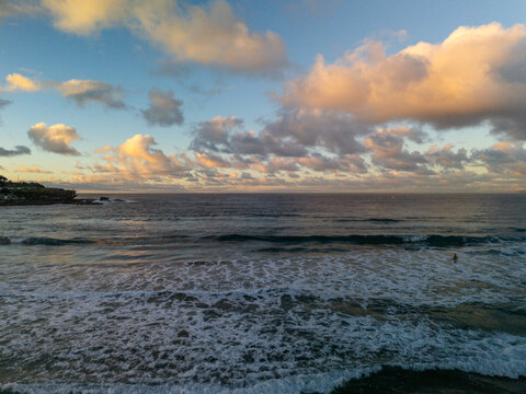 Bondi Beach in early morning with beautiful dramatic sky before sunrise. Swimmer stands in silhouette in foreground