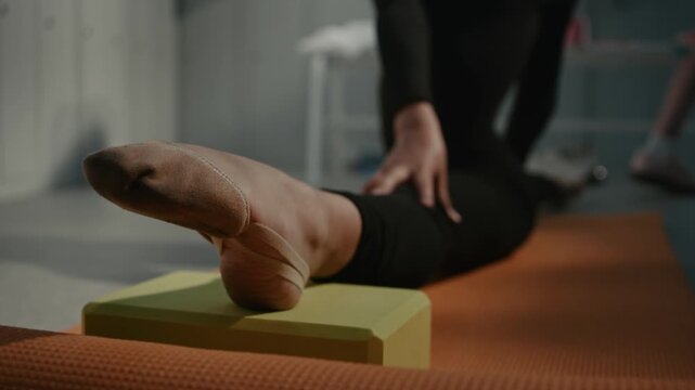 Close Up of Teenage Foot Wearing Traditional Demi pointe Toe Shoe While Resting on EVA Foam Yoga Brick. Intense Ankle Flexibility Required For Professional Competitive Gymnastics. Stretching Routine.