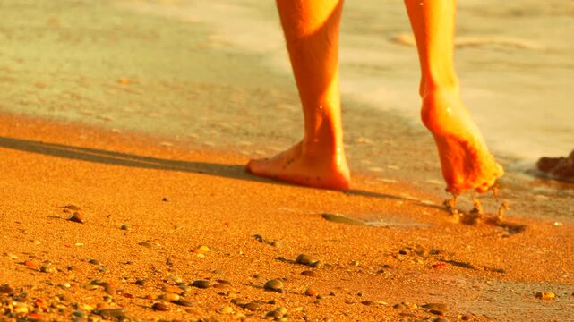 Feet beach walking, bare legs on golden sand by ocean shore at sunset, tranquil vacation travel