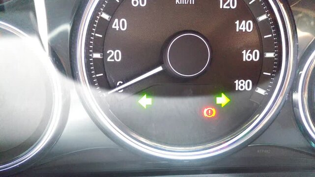 Car dashboard clearly displays the hazard lights flashing and handbrake sign on
