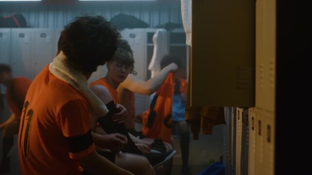 Group of Young Football Players Relaxes in Modern Team Locker Room. While Changing into Casual Clothes, Teammates Play Around, Exchange Jokes. Youth Sports Culture and Positive Team Relationships.