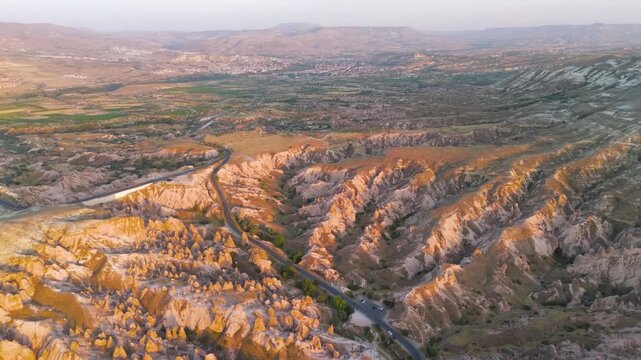 Goreme, Nevsehir, Turkey. Devrent Valley, eroded volcanic tuff formations and a winding road cutting through the dramatic ridges, aerial panoramic view at golden hour sunset. Aerial View