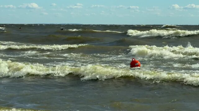 Red navigation buoy bobbing on waves in a bay, rough water conditions, coastal safety marker, windy weather, marine navigation concept.