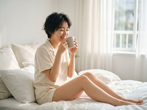 明るい寝室のベッドの上でショートヘアのパジャマ姿で寛ぐ女性