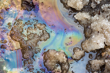 Obraz premium Iridescent sheen from oils and fuels on melting snow and puddles, spring thaw, environmental pollution