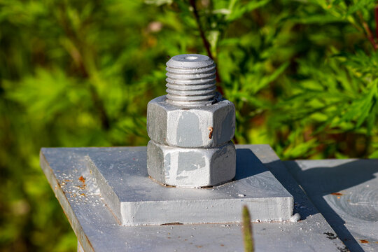 Close-up of a heavy-duty industrial steel bolt and nut fastening a high-voltage power transmission tower base on a sunny day with soft green natural blurred background
