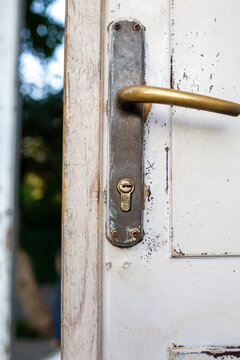 Old brass door handle on weathered white wooden door with peeling paint, vintage architecture detail