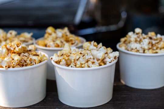 Fresh popcorn served in white paper cups lined up outdoors, snack food catering display
