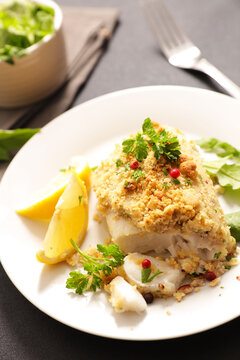 Baked fish fillet with herb crumble crust and lemon on plate