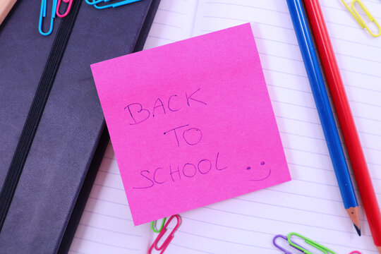 Back to school handwritten note on pink sticky paper with supplies