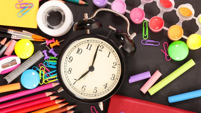Alarm clock with colorful school supplies on blackboard background, back to school concept