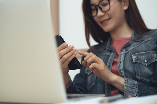 Smiling asian woman using smartphone for social media networking with laptop on cafe table during working remotely, business casual, modern lifestyle