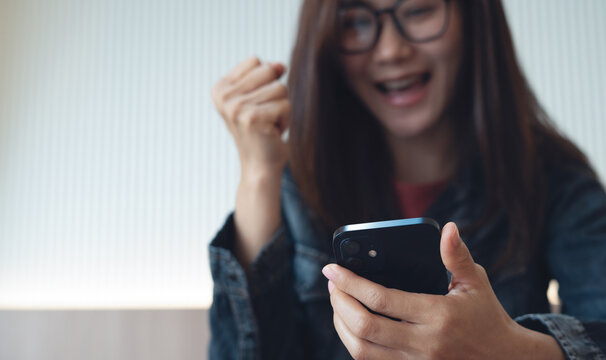 Asian young woman looking mobile phone cheerfully and feel excited with good news or discount voucher for shopping online at home. 