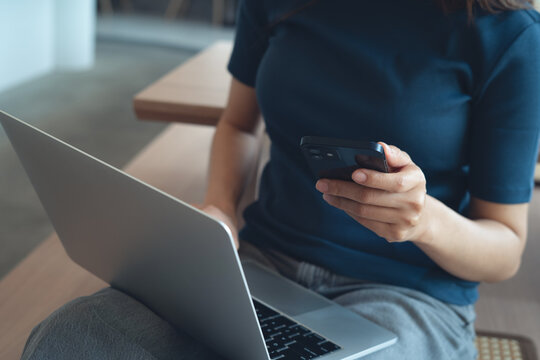 Woman sitting on the floor, using smartphone, remote working on laptop on her lap at home. digital nomad, online job, freelance lifestyle