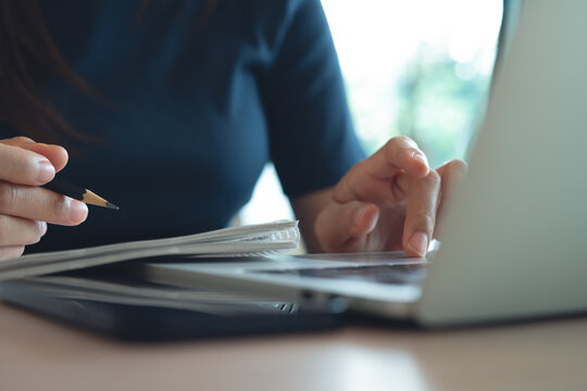 Woman using laptop searching and writing in notebook, remote working at home, close up. surfing the net, online study 