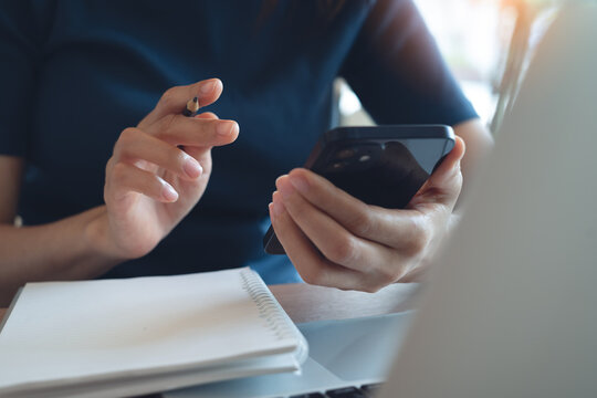 Woman using smartphone searching the information with notebook on table, remote working or online studying at home