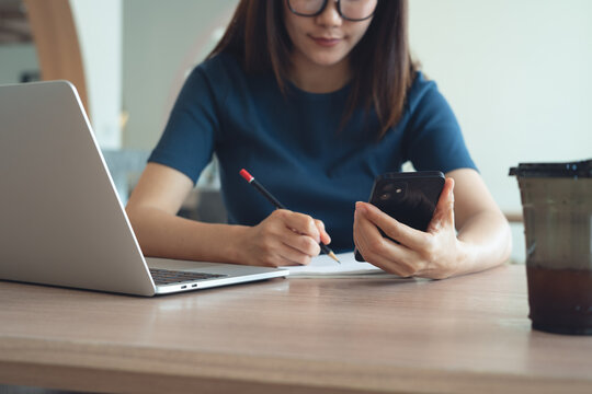 Young asian woman using smartphone and laptop, remote working or online studying and writing n notebook at modern workspace, digital nomad lifestyle, business casual